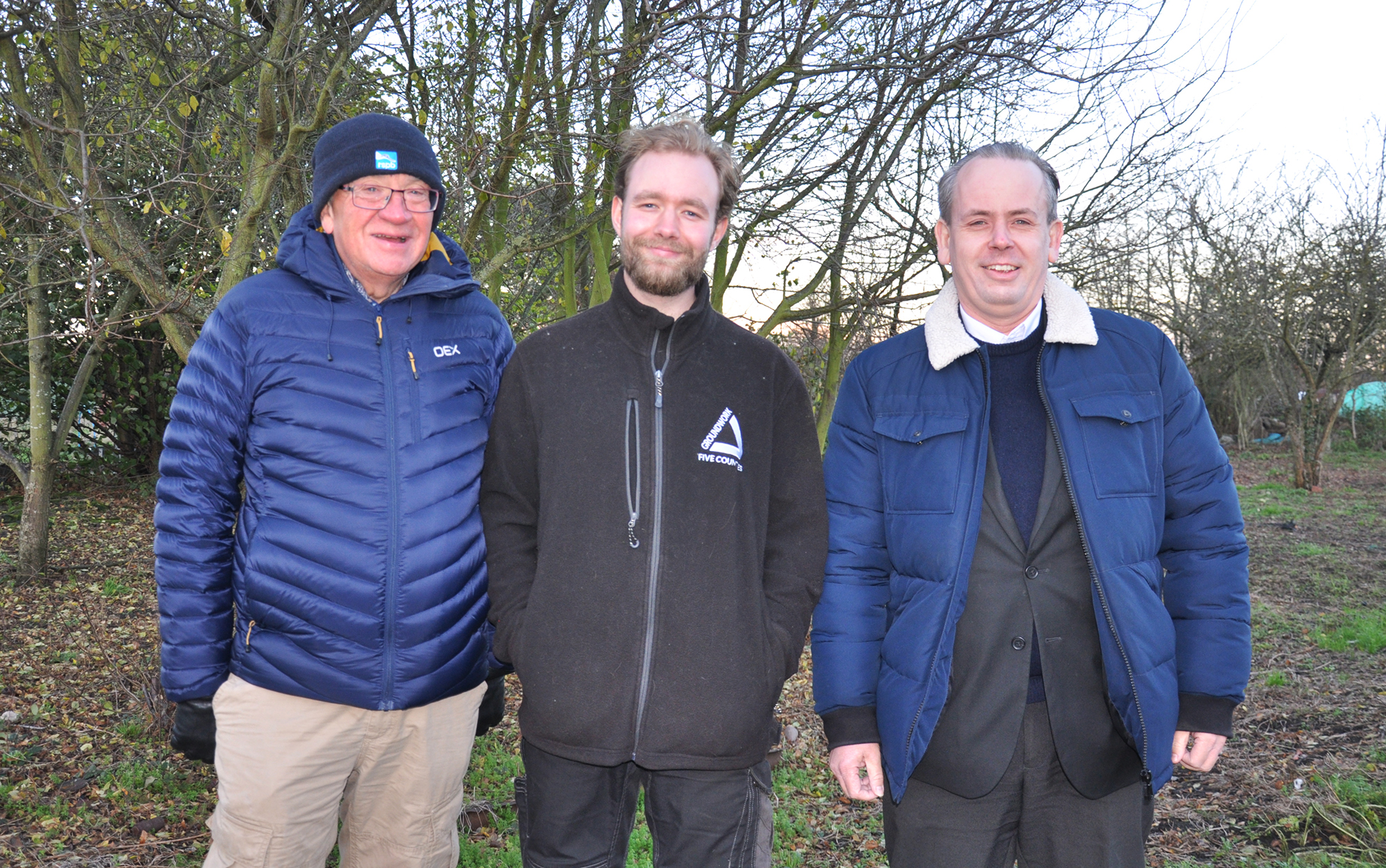 Three men smiling at camera in outdoor setting.