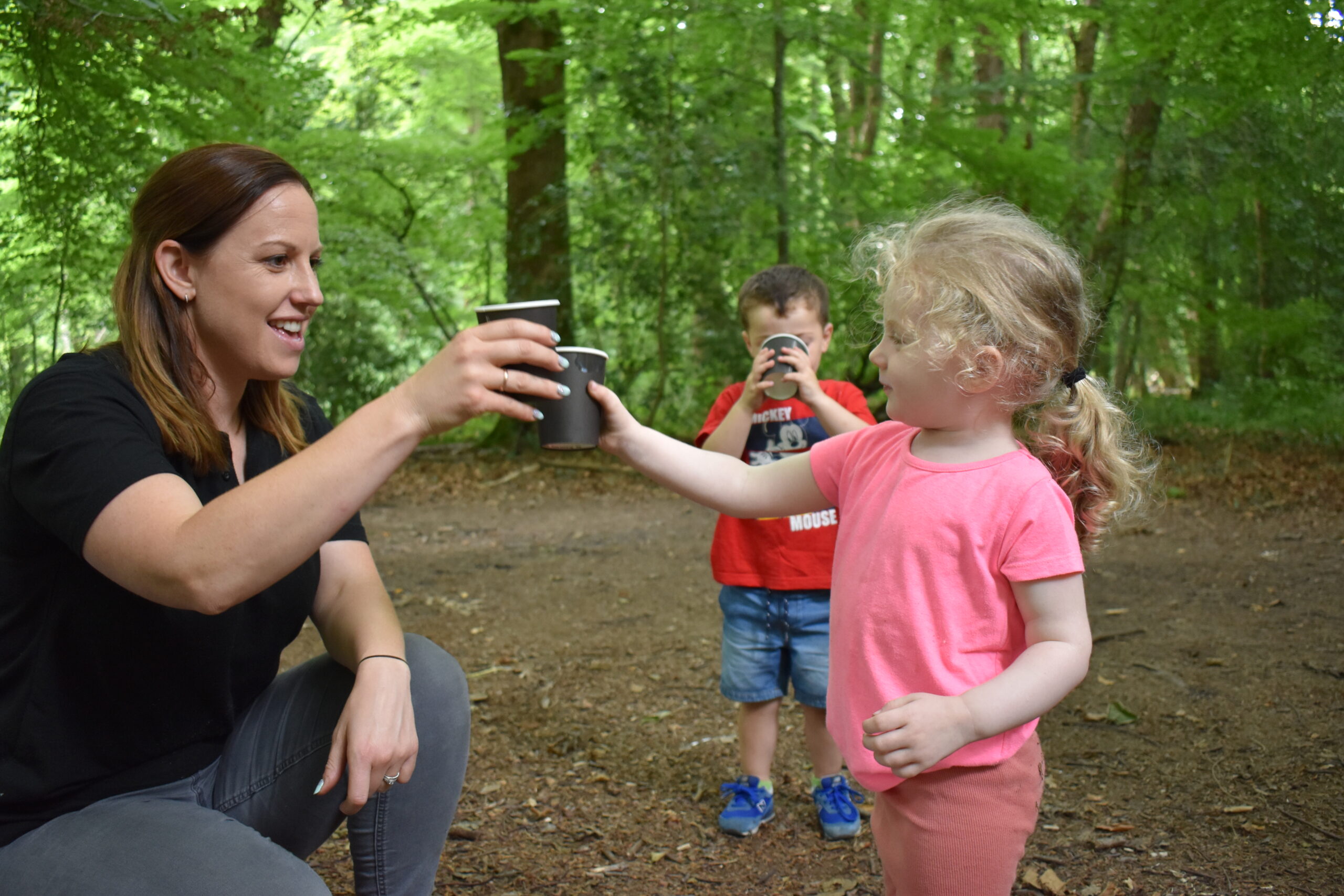 Woman and two children in a forest drinking from plastic cups