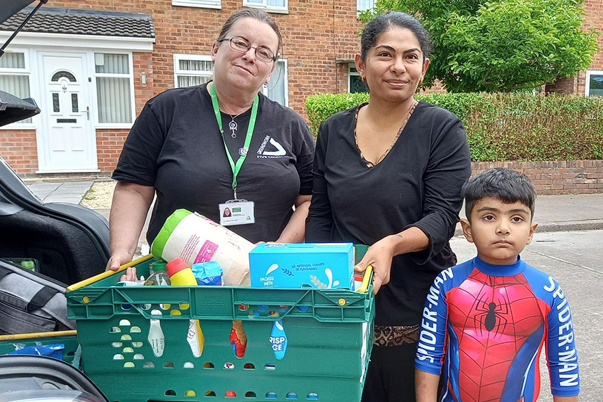 Two woman holding green plastic basket with food items, young boy in Spiderman costume standing next to them.