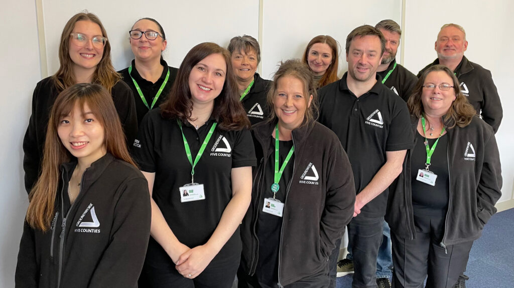 Group of people wearing black branded tops with white Groundwork logo, smiling at camera.