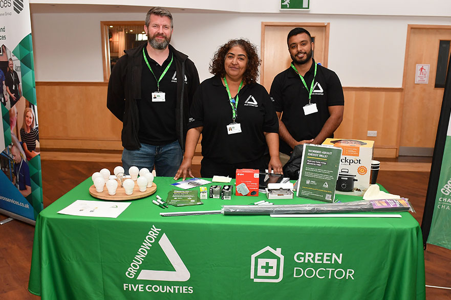 Two men and a woman in black T-shirts behind table with green table cloth and logos for Green Doctor and Groundwork Five Counties