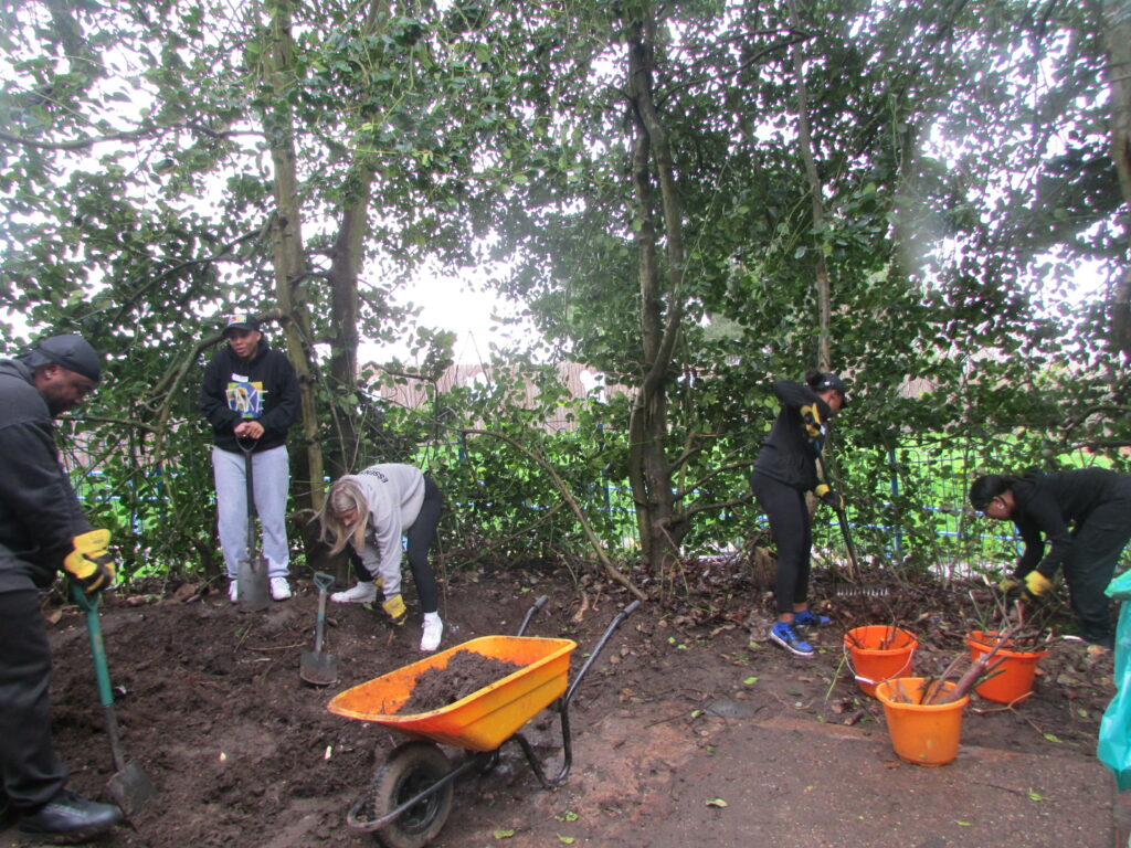 Photo of volunteer workers at the Annie Lennard Primary School, shovelling dirt into a wheelbarrow and landscaping tree branches into buckets.