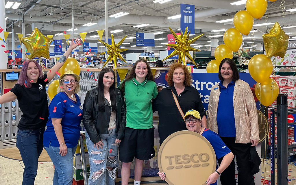 Group of people in Tesco store with gold balloons and large gold coin