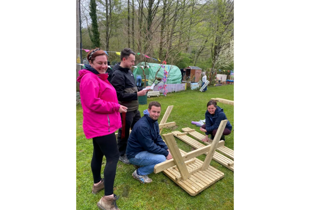 Four volunteers in a park assembling a wooden bench as part of a corporate activity day.