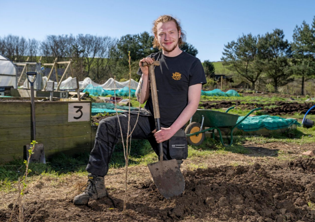 Photo of a man who is kneeling down and holding a shovel.